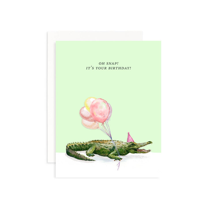 Birthday card with a crocodile holding balloons and a party hat on a light green background.