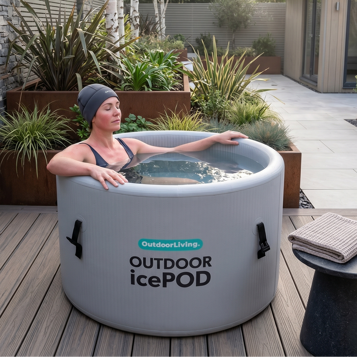 Woman relaxing in an inflatable ice pod outdoors on a wooden deck with plants and a building in the background.