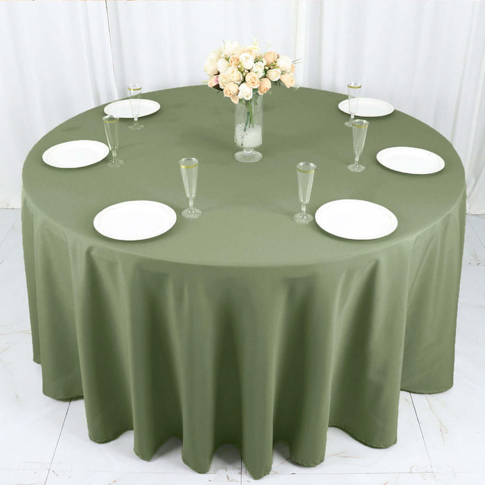 Round olive green tablecloth with white dinnerware and a floral centerpiece.