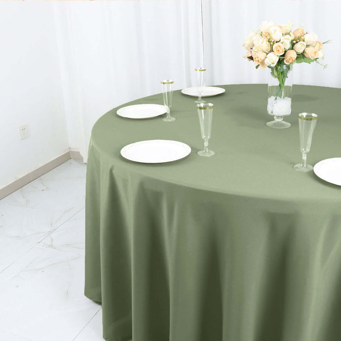 Round olive green tablecloth draped over a round table set for dining.