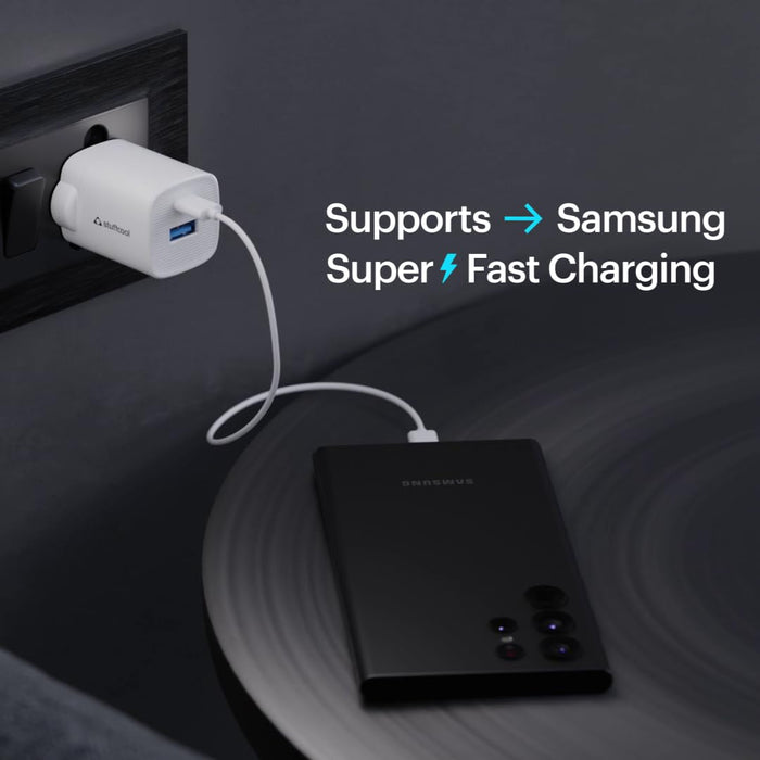 A black portable power bank with a white cable plugged into a white USB charger, shown on a dark surface with text that says it supports Samsung super fast charging.