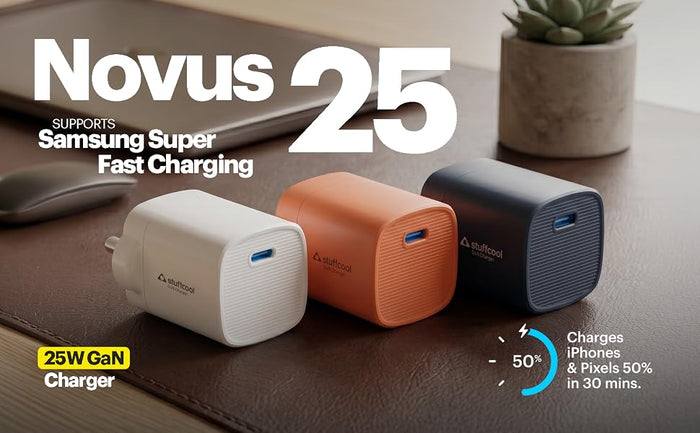 Three small Novus 25 25W GaN chargers in white, orange, and dark blue-gray are shown on a brown desk surface with promotional text, including 'SUPPORTS Samsung Super Fast Charging' and 'Charges iPhones & Pixels 50% in 30 mins.'.