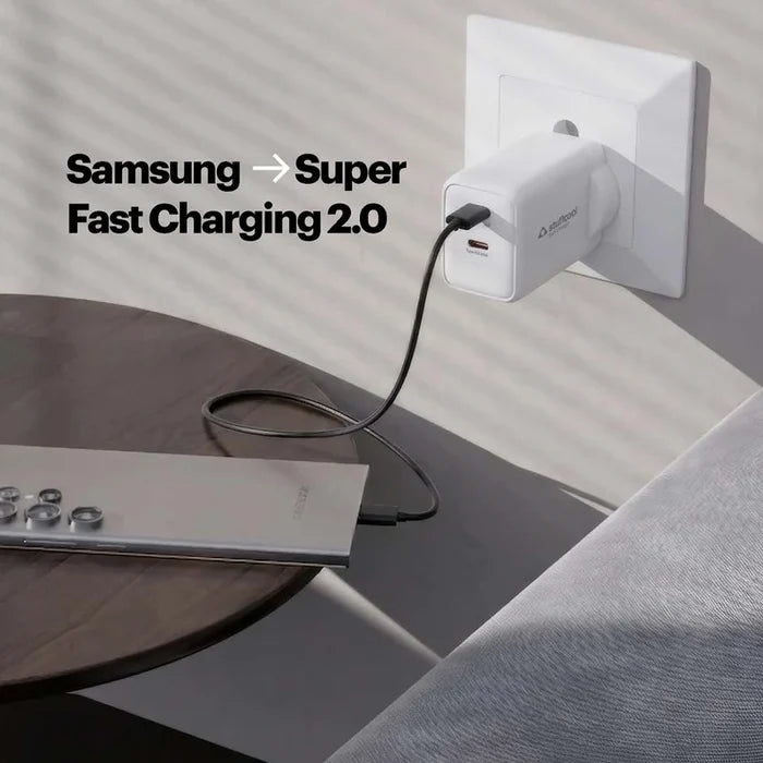 A white Pixelpower USB-C fast charger plugged into a wall outlet, charging a silver laptop on a dark wooden table. Text on the image reads 'Samsung -> Super Fast Charging 2.