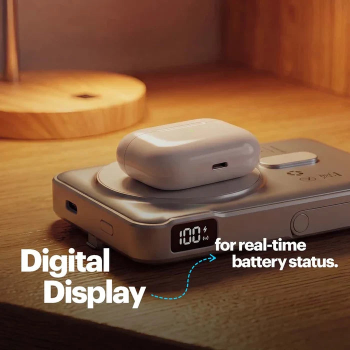 A silver electronic battery/power bank device sits on a wooden surface with a white wireless earbud case resting on top. The device has a small digital display showing 100% battery, and overlaid text reads 'Digital Display' and 'for real-time battery status.